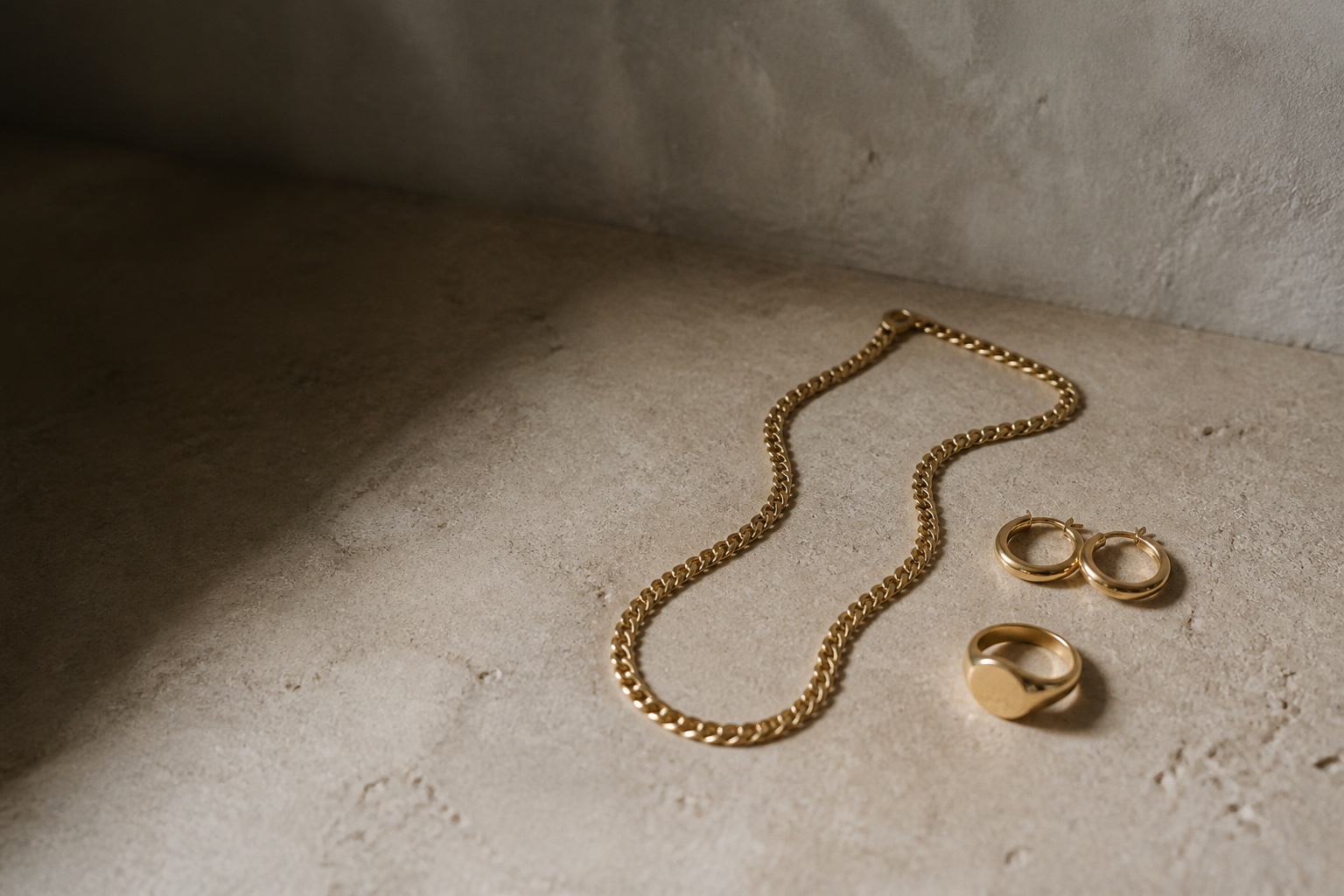 Fine gold chain, hoop earrings and signet ring arranged on limestone